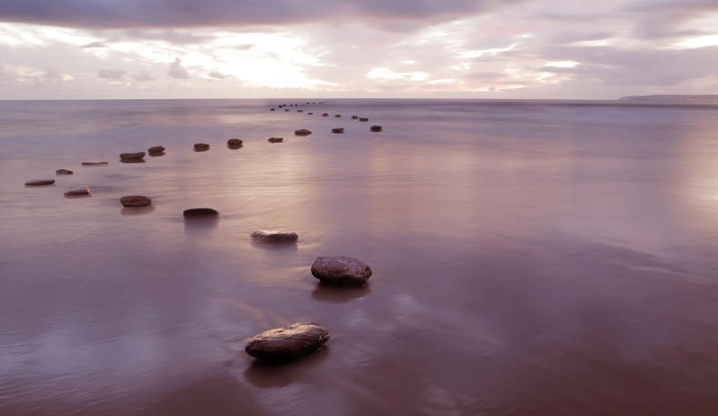 Blick aufs Meer bei Dämmerung. Steine im flachen Wasser bilden eine Art Brücke ins meer hinein